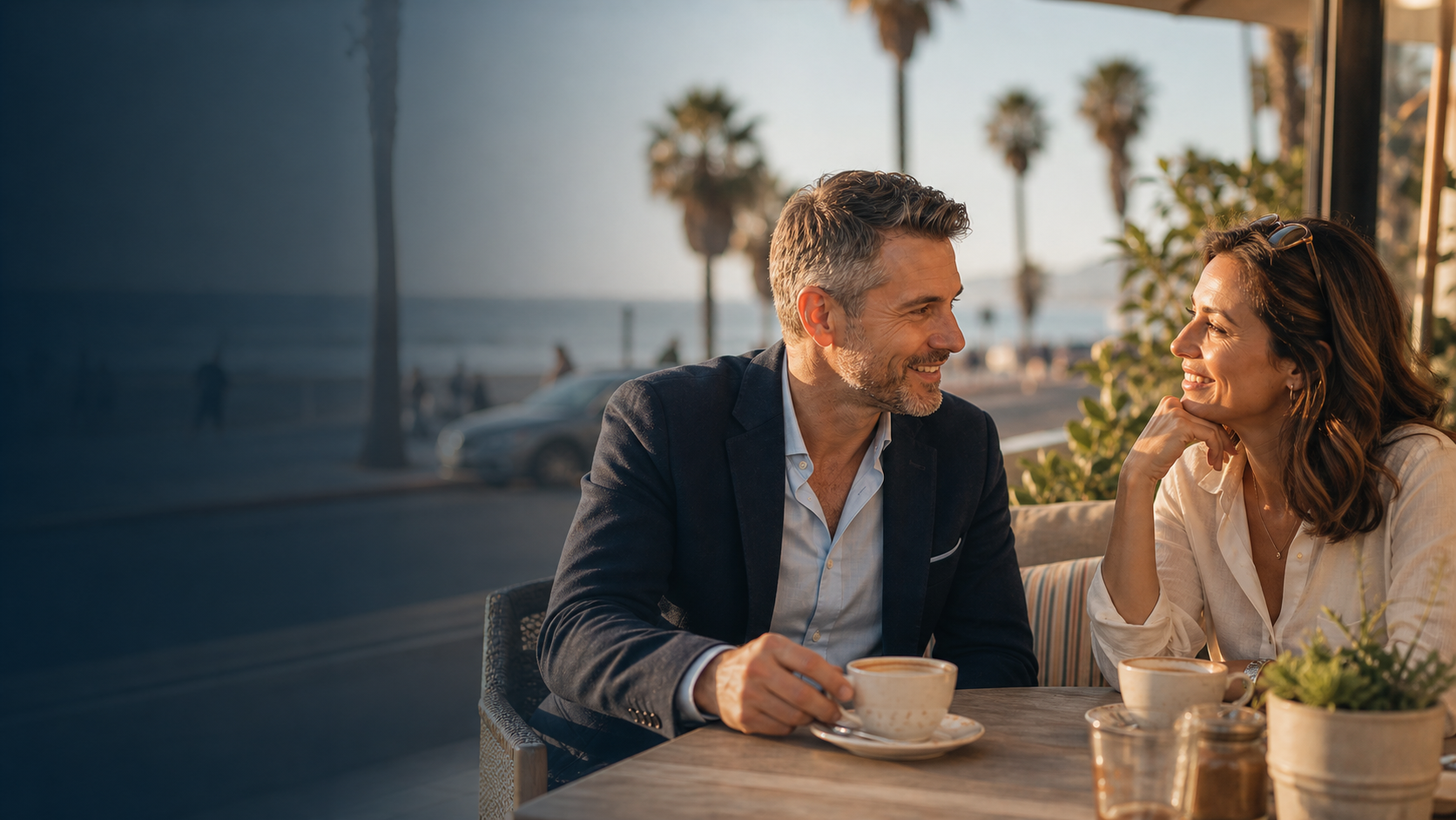 Two Los Angeles singles talking at a Santa Monica outdoor cafe near palm trees and the coast